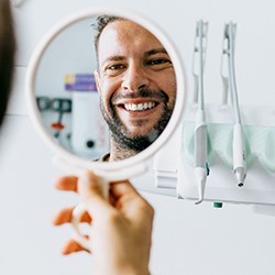 man smiling in mirror at dentist 