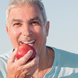 man eating an apple and enjoying the health benefits of dental implants in Owings Mills