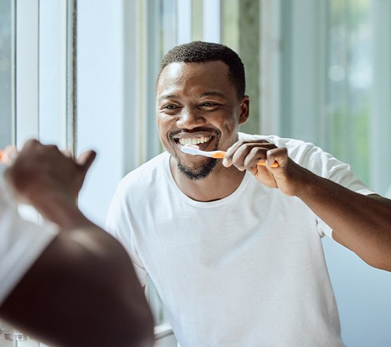 Man smiling while brushing his teeth