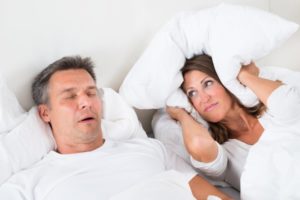 a man asleep and snoring and a woman covering her ears with a pillow