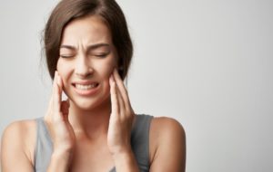 a young female wearing a gray tank top and holding her jaw while cringing in pain