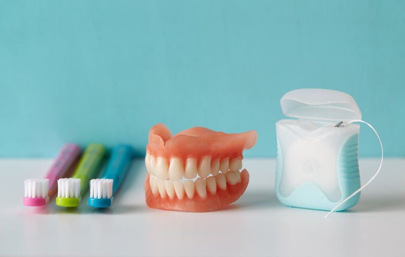 Dentures on cabinet with toothbrush and dental floss
