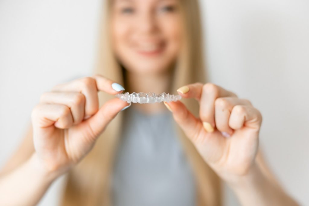 Closeup of patient smiling while holding Invisalign aligner