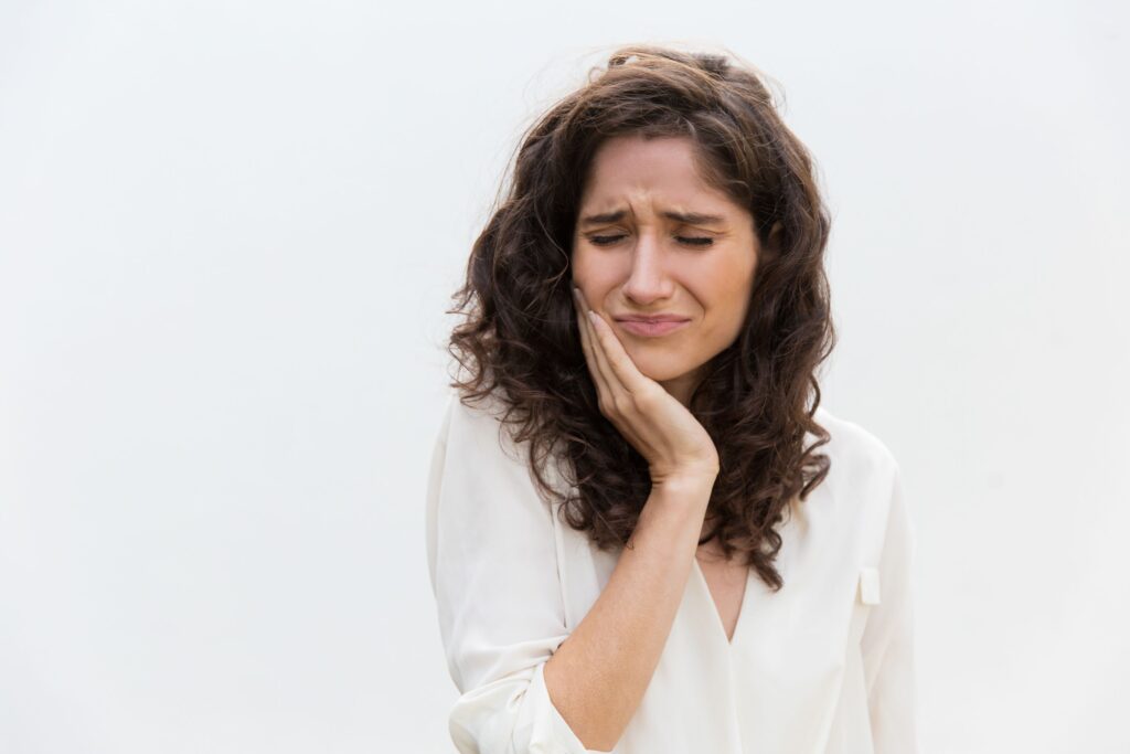 Woman with brown hair in white shirt pressing hand to jaw in pain