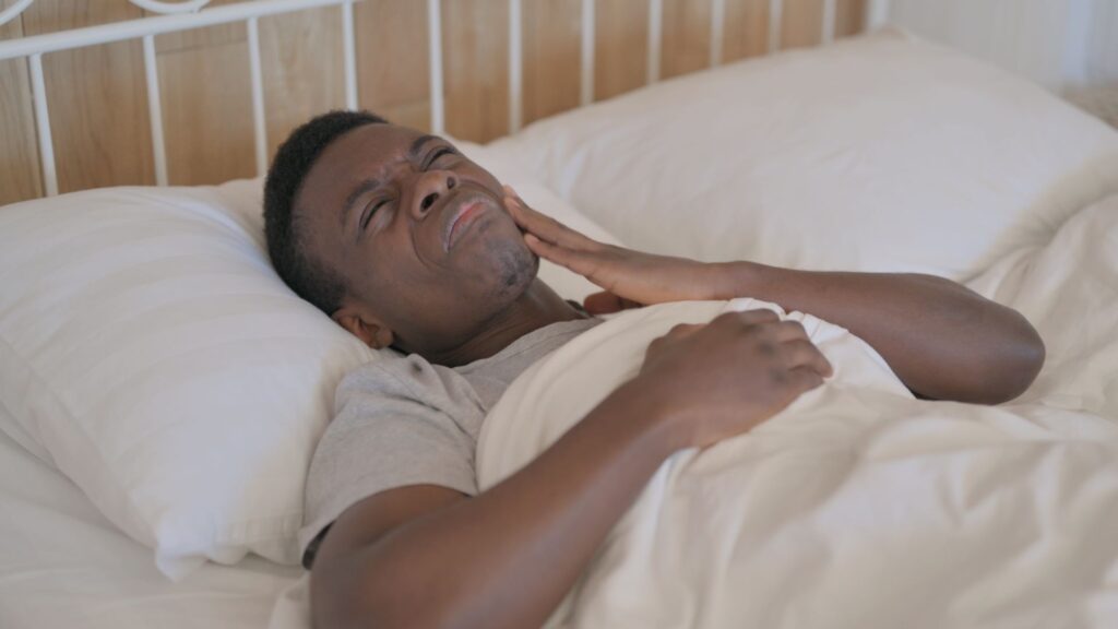 Man in bed holding hand to jaw in pain